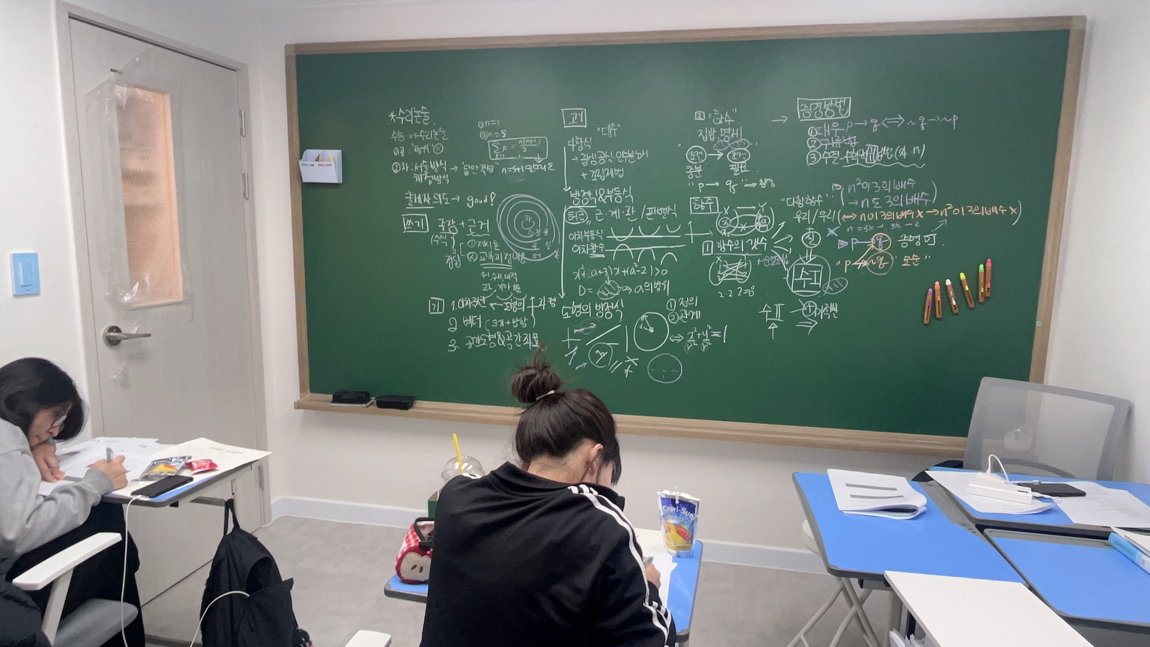 칠판 앞 소수정예 수리논술 수업에서 학생들이 답안을 작성하는 모습